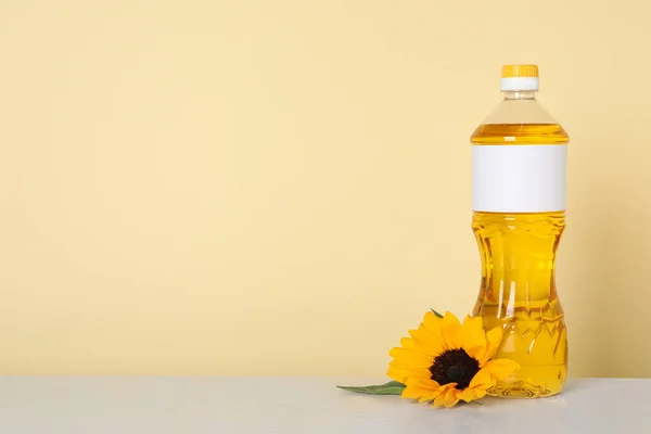 Bottle of cooking oil and sunflower on white table, space for text