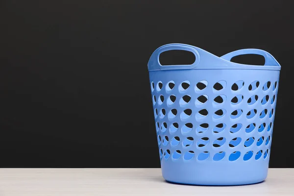 Empty plastic laundry basket near dark grey wall. Space for text