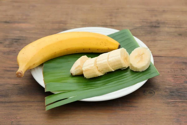 Plate with delicious bananas and fresh leaf on wooden table