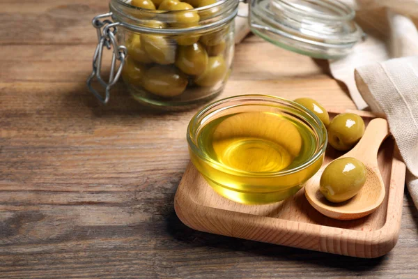 Bowl of cooking oil and olives on wooden table. Space for text