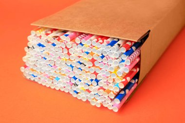 Box with many paper drinking straws on orange background