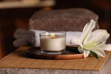 Spa composition with burning candle, lily flower and towels on massage table in wellness center