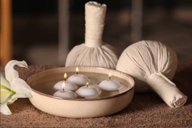 Spa composition with burning candles, lily flower and herbal bags on massage table in wellness center, closeup