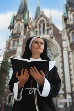 Young nun reading Bible near cathedral outdoors
