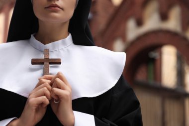 Young nun holding Christian cross near building outdoors, closeup