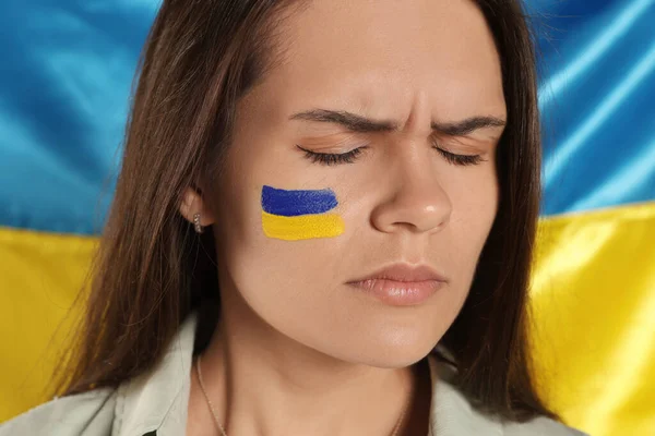 Sad young woman with face paint near Ukrainian flag, closeup