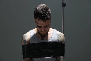Man with bruise taped up and taken hostage on grey background