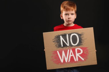 Boy holding poster No War against black background, space for text