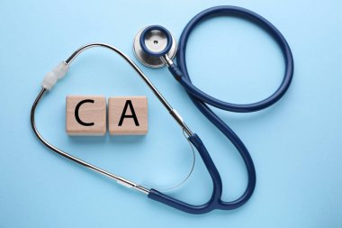 Stethoscope and calcium symbol made of wooden cubes with letters on light blue background, flat lay