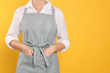 Woman in clean apron with pattern on orange background, closeup. Space for text