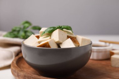 Bowl of smoked tofu cubes and basil on wooden tray, closeup