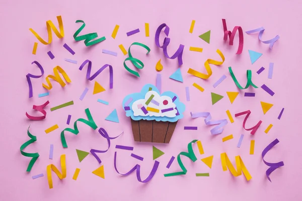 Birthday party. Paper cupcake and confetti on pink background, flat lay