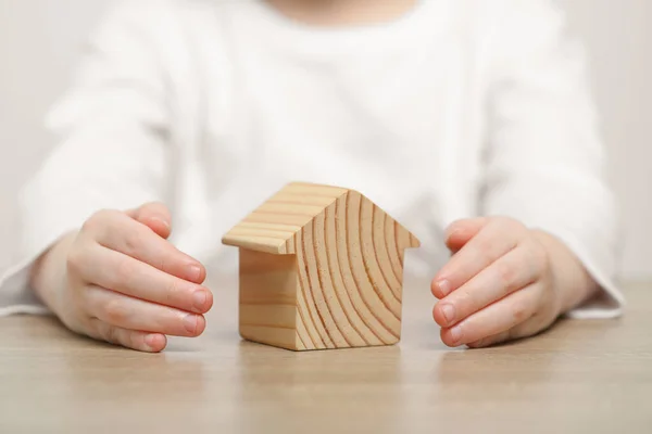 Home security concept. Little child with house model at wooden table, closeup