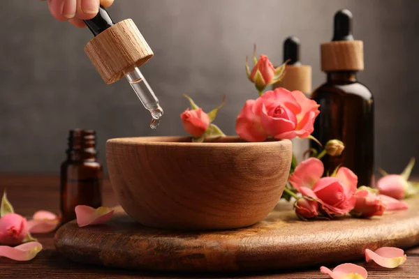 Woman dripping essential oil into bowl at wooden table, closeup. Aromatherapy treatment