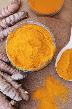 Glass jar of turmeric powder and roots on wooden table, flat lay