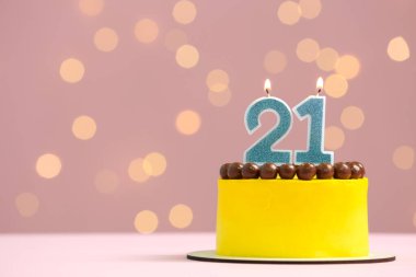 Coming of age party - 21st birthday. Delicious cake with number shaped candles on pink background against blurred lights, space for text