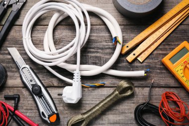 Wires and electrician's tools on wooden table, flat lay