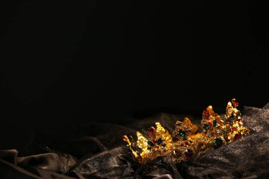 Beautiful golden crown with gems on dark cloth. Space for text