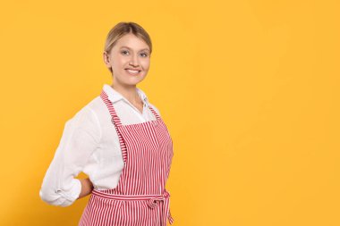 Beautiful young woman in clean striped apron on orange background. Space for text