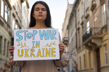 Sad woman holding poster Stop War in Ukraine on city street