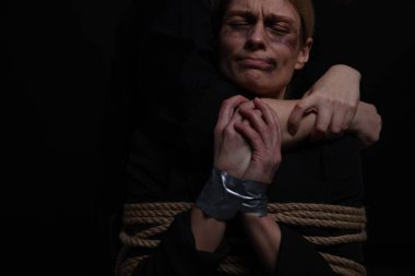 Kidnapper restraining woman on dark background, closeup with space for text. Taking hostage