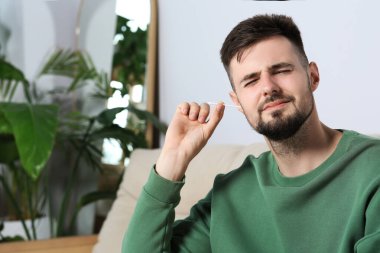 Young man cleaning ear with cotton swab at home. Space for text