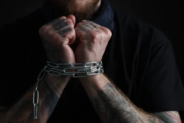 Man with chained hands on dark background, closeup. Hostage