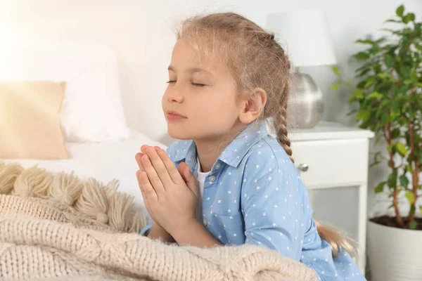 Girl with clasped hands praying near bed at home