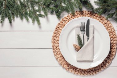 Beautiful festive place setting with cutlery and fir branches for Christmas dinner on white wooden table, flat lay. Space for text