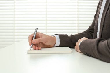 Beyaz masadaki defterde yazan adam kapalı, yakın plan.