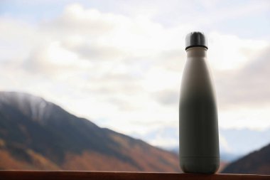 Thermo bottle on wooden surface in beautiful mountains. Space for text
