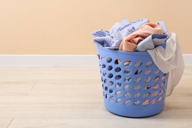 Laundry basket with clothes near beige wall indoors. Space for text