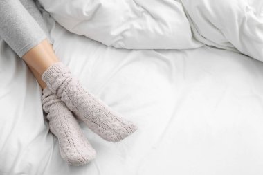 Woman wearing warm socks in comfortable bed, closeup. Space for text