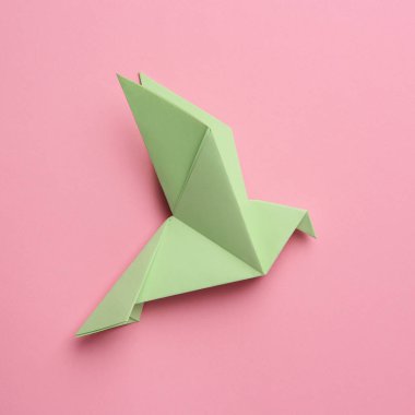 Beautiful light green origami bird on pink background, top view