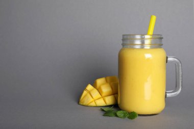 Mason jar of tasty smoothie with straw, mango and mint leaves on grey background. Space for text