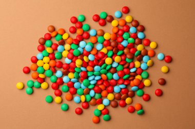 Tasty colorful candies on light brown background, flat lay