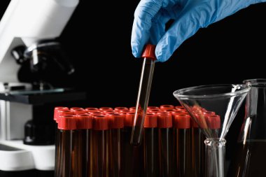 Scientist taking test tube with brown liquid from stand, closeup