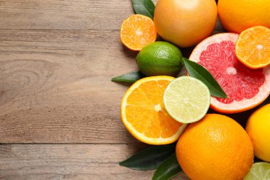 Different ripe citrus fruits with green leaves on wooden table, above view. Space for text