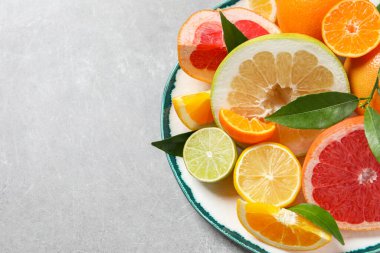 Plate with different citrus fruits and fresh leaves on light grey table, top view. Space for text