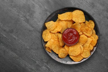 Delicious chips with ketchup on grey table, top view. Space for text
