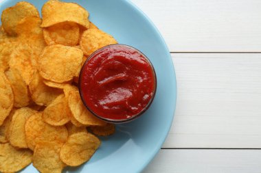 Delicious chips with ketchup on white wooden table, top view. Space for text