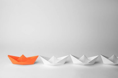 Group of paper boats following orange one on white background. Leadership concept