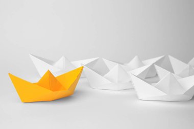 Group of paper boats following orange one on white background. Leadership concept