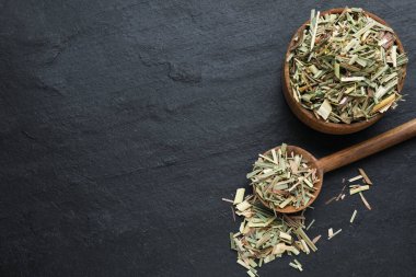 Wooden bowl and spoon with aromatic dried lemongrass on black table, flat lay. Space for text