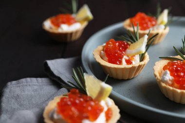 Delicious tartlets with red caviar and cream cheese served on wooden table, closeup