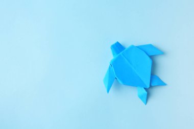 Origami art. Handmade bright paper turtle on light blue background, top view with space for text