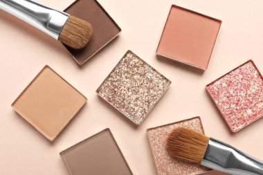 Different beautiful eye shadows and makeup brushes on beige background, flat lay