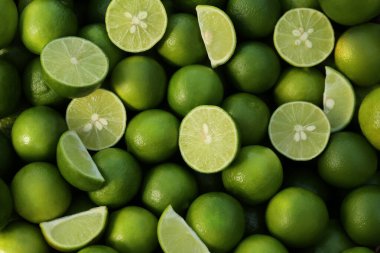 Whole and cut fresh ripe green limes as background, top view
