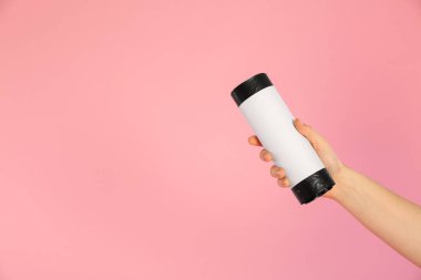 Woman holding roll of black garbage bags on pink background, closeup. Space for text