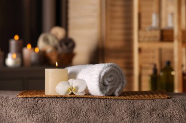 Spa composition with candle, orchid flower and rolled towel on massage table in wellness center, space for text